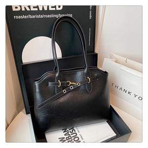 Close-up of black tote bag featuring fine leather texture and elegant gold metal buckles