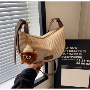 Detail of woven crescent bag with brown leather strap and plush monster charm