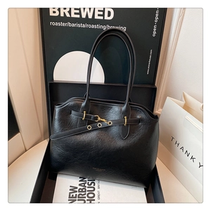 Detail of black tote bag featuring gold buckle and branding in a stylish gift box