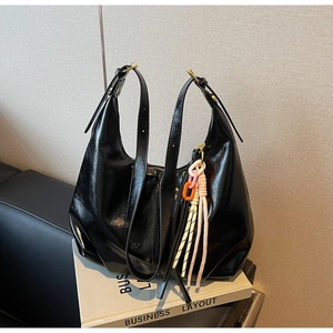 Détail du sac hobo en cuir verni noir avec charm tissé coloré sur canapé en cuir