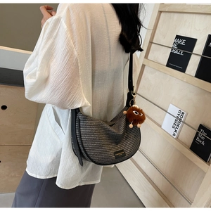 Detail of woven crescent crossbody bag with black leather logo and plush toy charm