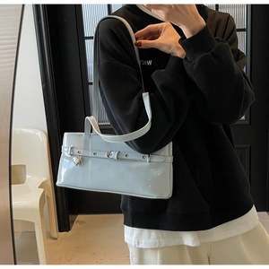 Close-up of light blue patent leather underarm bag with decorative belt buckle and heart charm