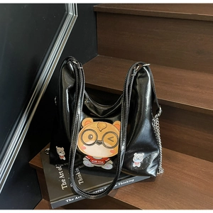 Detail of black glossy tote bag featuring a cartoon bear patch and white contrast stitching