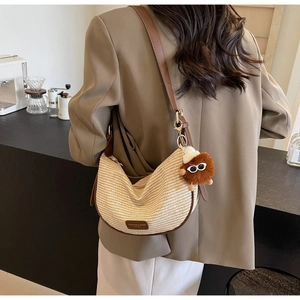 Detail of beige woven half-moon bag with brown leather trim and plush charm