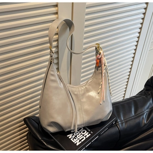 Détail d'un sac hobo gris clair avec pompon et breloques décoratives colorées