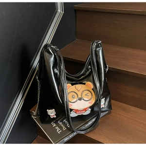 Detail of black patent leather tote bag featuring a cartoon bear embroidery and white stitching