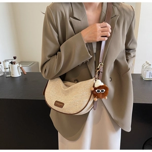 Detail of woven crescent bag with brown leather trim and a cute plush monster charm