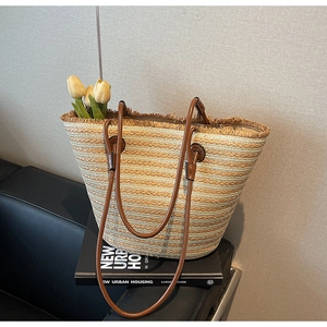 Close-up of striped straw tote bag with fringe edge and leather straps on a book