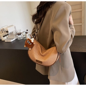 Detail of straw-textured half-moon shoulder bag with leather trim and plush pendant