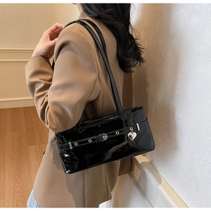 Detail of black glossy patent leather shoulder bag with a metal heart pendant