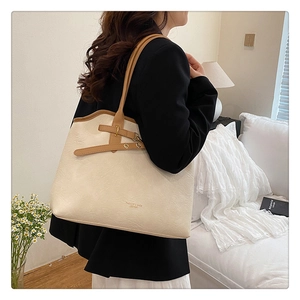 Detailed view of beige faux leather tote bag with brown straps worn by a model in soft light