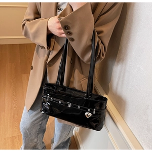 Close-up of black patent leather underarm bag with silver heart charm and metal buckles
