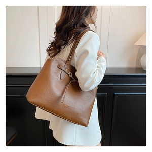 Detail of caramel tote bag with metallic buckle and embossed logo on soft leather texture