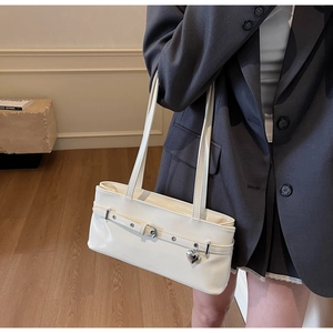 Close-up of white shoulder bag with heart pendant and buckle detail worn with a suit