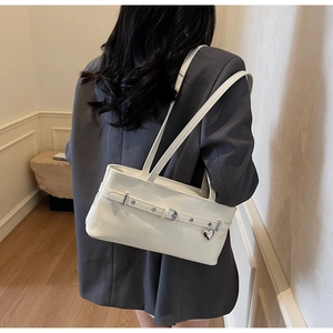 Detail of white glossy underarm bag with metal heart charm and rivet belt on model