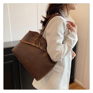 Close-up of brown leather tote bag with gold metal buckle and embossed brand text