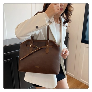 Detail of dark brown leather tote bag with gold hardware and fashion texture on a white suit