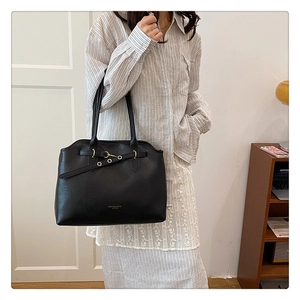 Detail of black leather tote bag with lychee texture and gold metal buckle accents