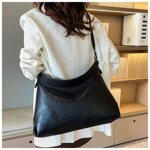 Detail of a large black dumpling tote with vintage pleated texture on a model