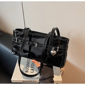 Detail of glossy black patent leather shoulder bag with silver heart pendant and buckle