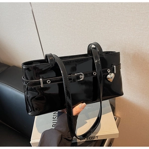 Close-up of black patent leather baguette bag featuring a silver heart charm and buckle