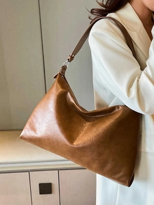Brown faux leather crescent hobo bag with wide shoulder strap worn with white suit