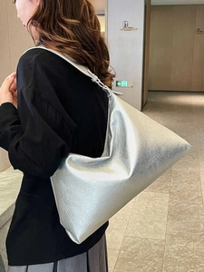 Silver metallic dumpling tote bag in pleated PU leather worn by a model in a hall