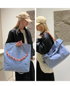 Détail du sac cabas bleu clair avec de larges anses tressées tricolores et texture en nylon