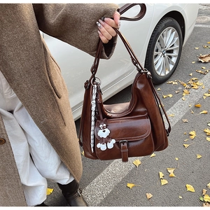 Detail of dark brown oil wax PU leather shoulder bag with white stitching and puppy charm