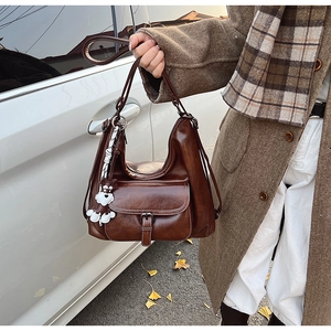 Close-up of vintage brown oil wax PU leather bag with plush bear charm in outdoor setting