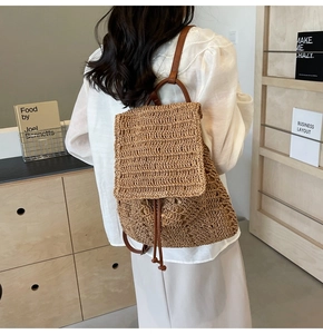 Detail of hand-woven straw backpack featuring brown leather straps in a minimalist setting