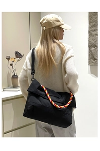 Détail d'un grand sac bandoulière noir avec poignée en corde tricolore porté par un mannequin