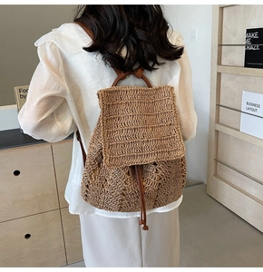Detail of straw woven backpack featuring brown leather straps and drawstring closure