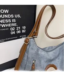 Dettaglio borsa hobo in denim blu con tracolla in pelle marrone e cuciture a contrasto