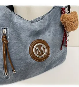 Dettaglio del logo M argento su cuoio marrone e ciondolo a orsetto sulla borsa blu