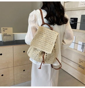 Detailed back view of a beige straw backpack with brown leather straps and drawstring flap