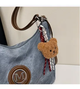 Dettaglio charm orsetto di peluche e logo M in metallo su borsa a spalla in denim blu