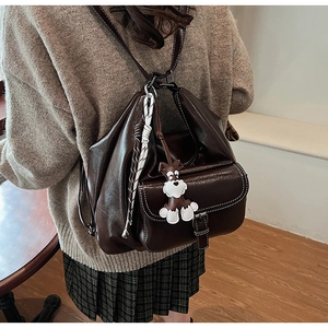 Detail of dark brown pebble leather backpack with white stitching and cartoon dog charm