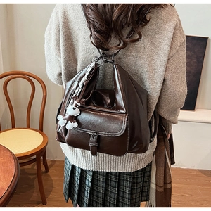 Detail of vintage brown leather backpack with contrast stitching and cartoon pendant charm