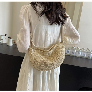 Dettaglio della borsa a tracolla beige tessuta a mano indossata con un abito bianco