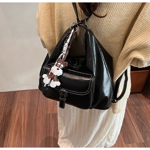 Detail of black glossy leather backpack featuring white stitching and puppy charm