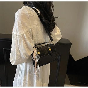 Dettaglio di una borsa a tracolla nera con borchie dorate e accessorio foulard in seta