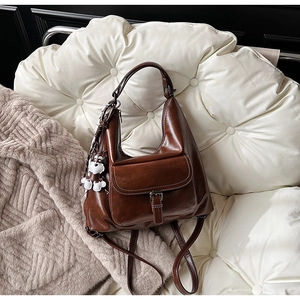 Detail of vintage brown leather shoulder bag with a cute white puppy pendant on a soft sofa