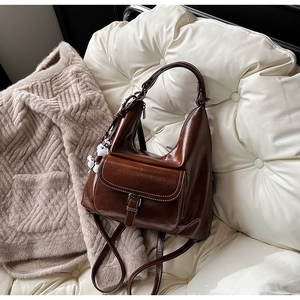Detail view of brown glossy leather backpack with white stitching and bear charm