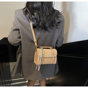 Dettaglio borsa a tracolla beige con fibbie dorate indossata su un abito grigio elegante