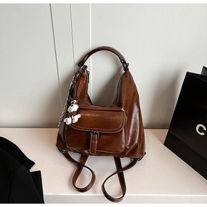 Detailed view of a vintage brown leather backpack with front flap pocket and bear charm