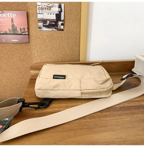 Close-up of beige nylon crossbody bag featuring a branded label on wooden surface