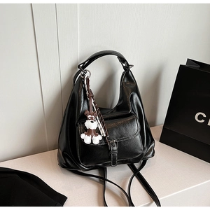 Close-up of black leather hobo bag with buckled pocket and a cute dog charm accessory