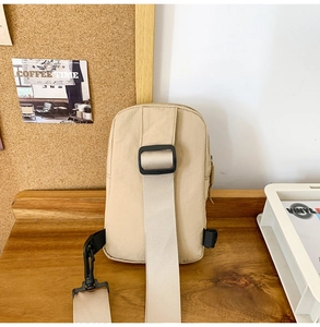 Detail of adjustable black buckle and woven strap on a beige nylon crossbody bag