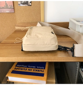 Detail of beige nylon crossbody bag with adjustable strap and metal zipper on wooden table